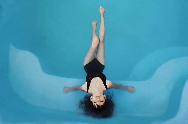 Žena v čiernych plavkách s čiernymi vlasmi leží v modrej vode.jpg