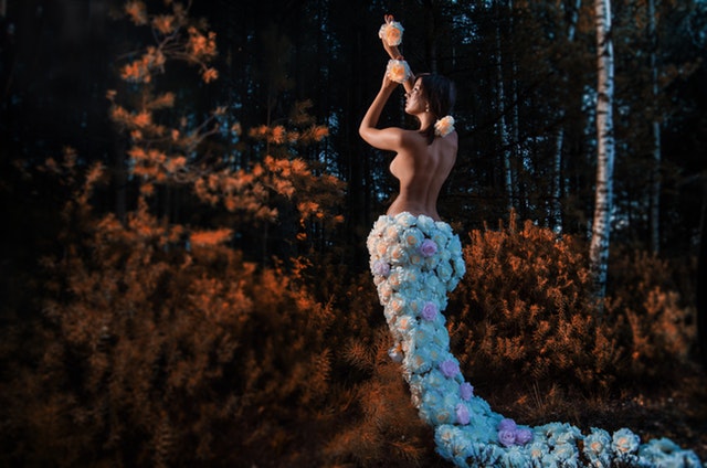 Žena v dlhej sukni z kvetov, hore bez, stojí pred lesom.jpg